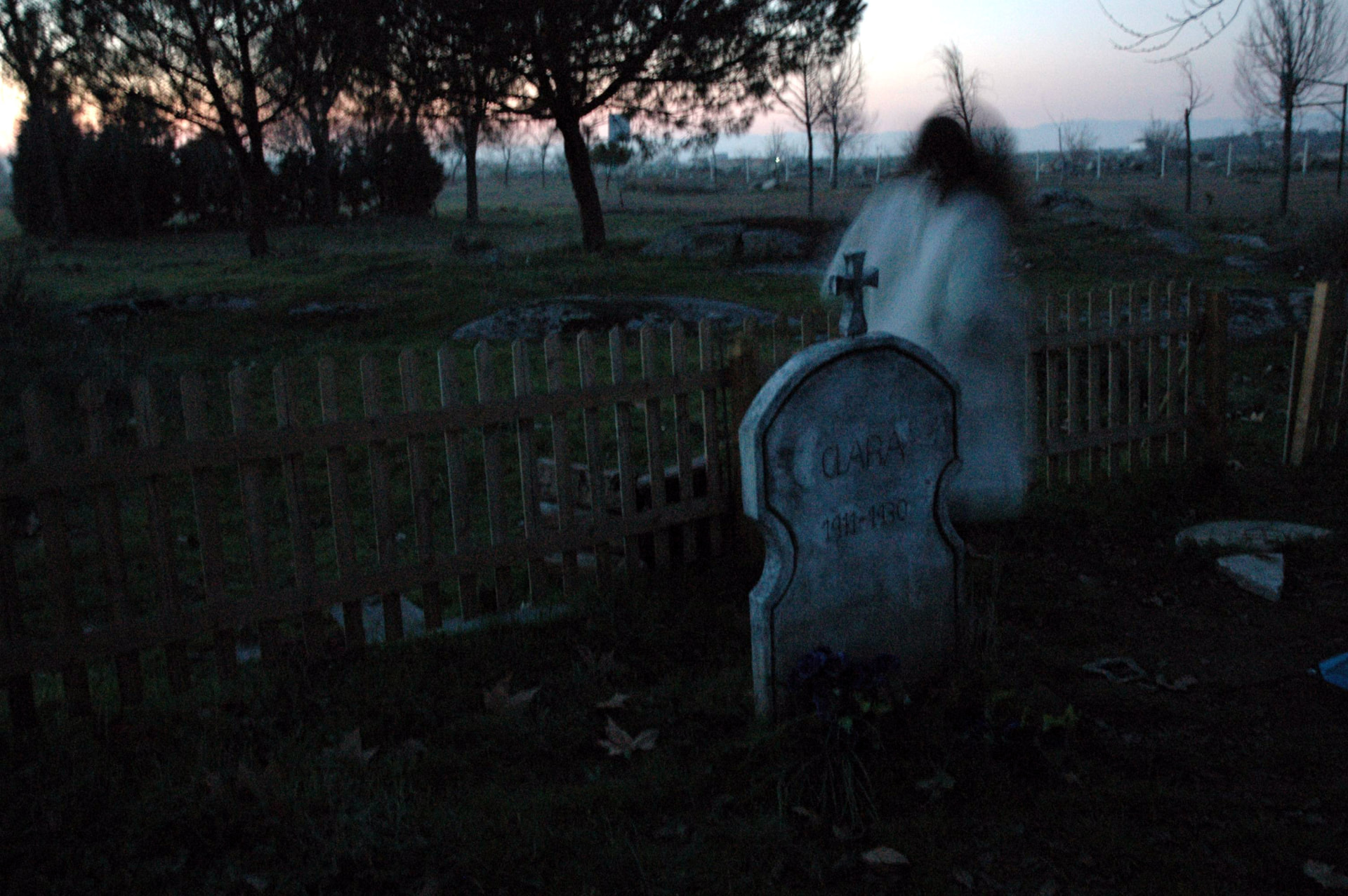 Figura fantasmal junto a una lápida en el cementerio familiar al anochecer